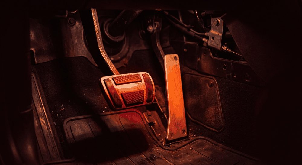 Dua pedal mobil menyala dalam kabin gelap: pedal rem bercahaya merah dan pedal gas bercahaya oranye